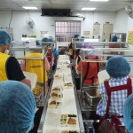 新業(yè)同仁與志工們繫上圍裙、套上防塵帽，戴上口罩，手捧一份份飯包各司其職，為的是準(zhǔn)時將熱騰騰的飯包送到長輩手中。