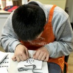 小羊苗朋友將臉湊近提袋上，仔細將貼紙慢慢地貼上，盡可能確保貼紙有貼正不歪斜。從肢體動作，可以曉得小羊們做每件事比別人費力，但不減心意。