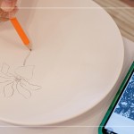筆尖在素色瓷胚上，輕輕滑過，對照著手機上的圖樣，描繪形塑出個人獨特的風(fēng)格。