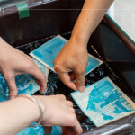 將明信片輕放入水箱中，清洗掉藥水後，隨著雙氧水的洗禮，藍(lán)曬圖像逐漸浮現(xiàn)。